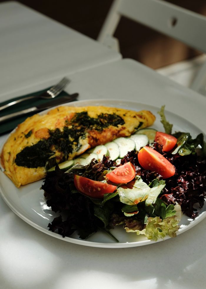 Close-up of a delicious omelette served with fresh salad greens and tomatoes on a white plate.